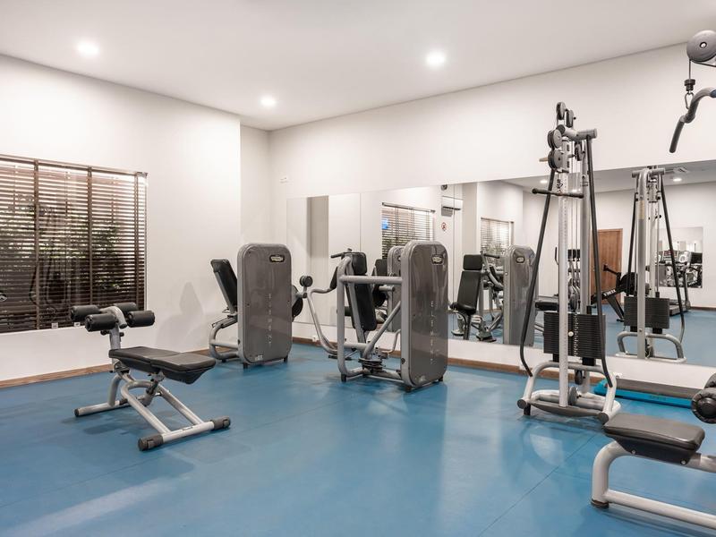 Moderne sportschool met blauwe vloer, fitnessapparaten, banken, spiegels en een groot raam.