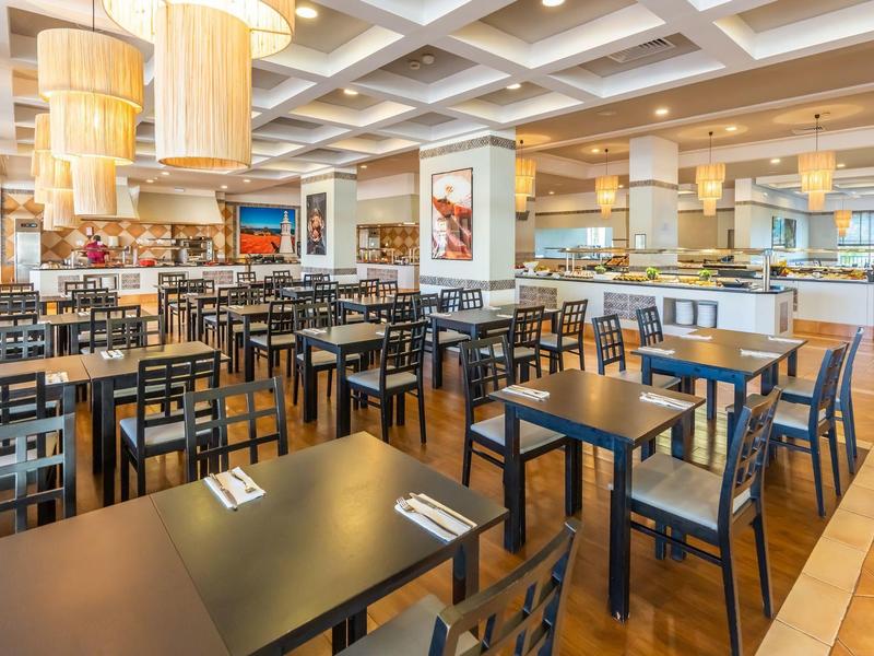 Ruim restaurantinterieur met meerdere tafels en stoelen, heldere verlichting en houten vloer.