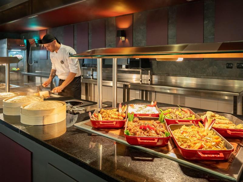 Chef in een keuken die buffetstijl eten bereidt met schalen friet en salade.