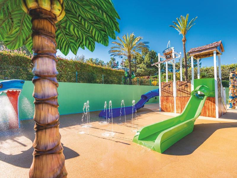 Zonnige buitenwaterspeeltuin met glijbanen, fonteinen en palmboomdecoraties.