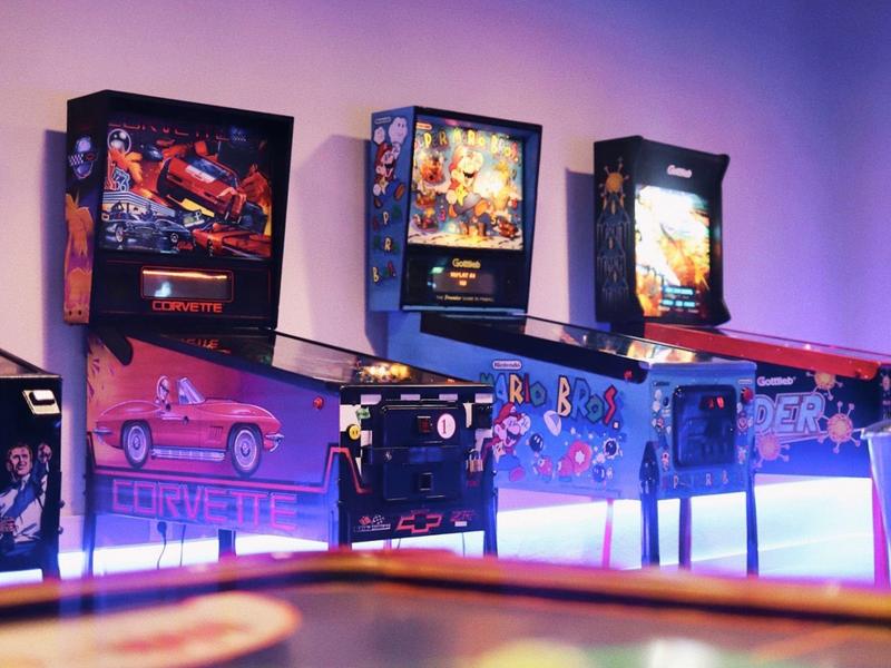 Rij met kleurrijke flipperkasten in een schemerige speelhal met paarse verlichting.