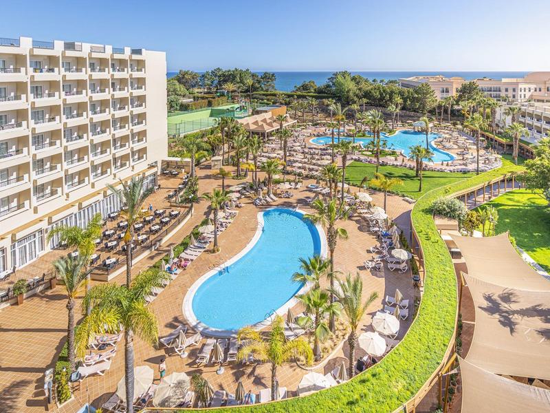 Resort met zwembaden, ligstoelen, palmbomen en zee op de achtergrond onder een heldere lucht.