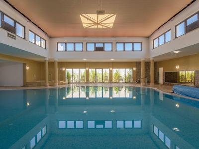 Großes Hallenbad mit klarem Wasser, hohen Fenstern und moderner Deckenbeleuchtung.