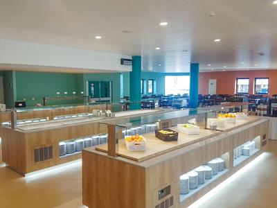 Großer, heller Selbstbedienungsbereich mit Holztheken und Glasvitrinen in moderner Kantine.