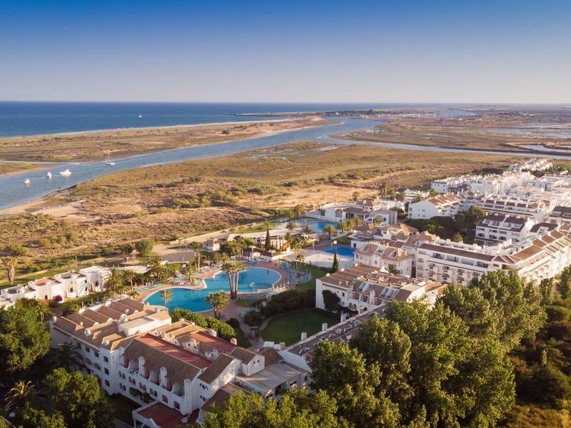 Große Ferienanlage mit mehreren Pools, umgeben von Büschen, nahe einem Fluss und offenem Meer.