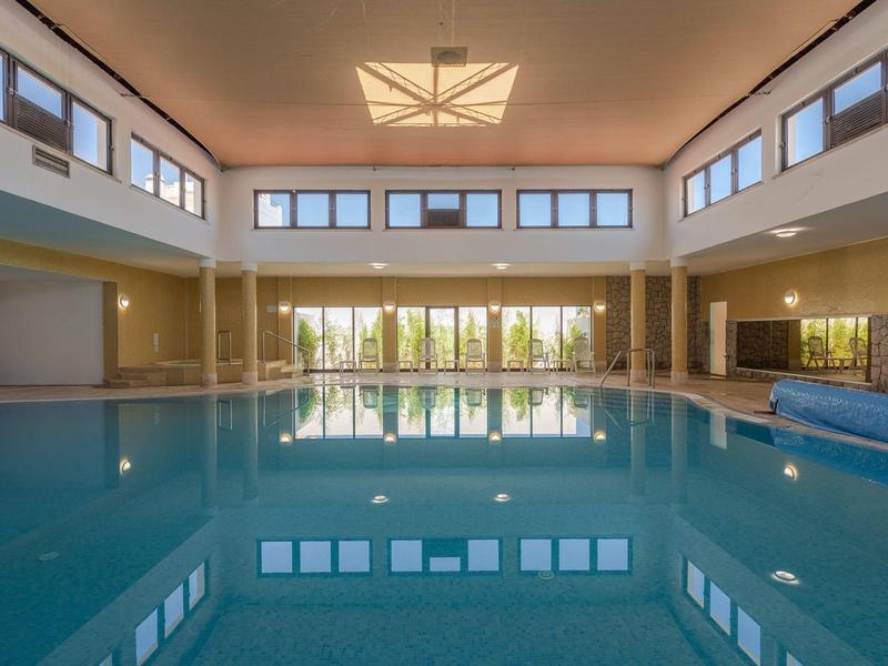 Großes Hallenbad mit klarem Wasser, hohen Fenstern und moderner Deckenbeleuchtung.