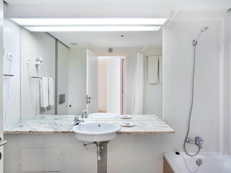 Helles, sauberes Badezimmer mit großem Spiegel, weißem Waschbecken, Badewanne und Handtüchern.