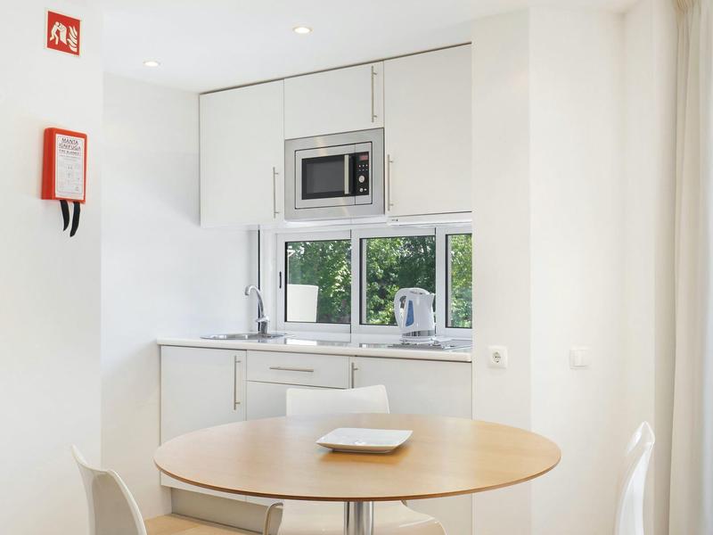 Helle, moderne Küche mit weißen Schränken, Mikrowelle, Fenster und rundem Holztisch mit Tellern.