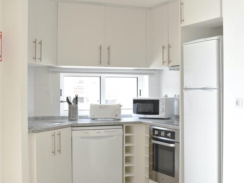 Kleine, moderne Küche mit weißer Einrichtung, grauen Arbeitsflächen und eingebauten Geräten.