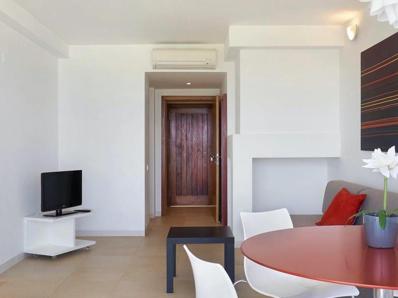 Moderner Wohnraum mit weißer Wand, rundem roten Tisch, Kamin und kleinem Fernseher.