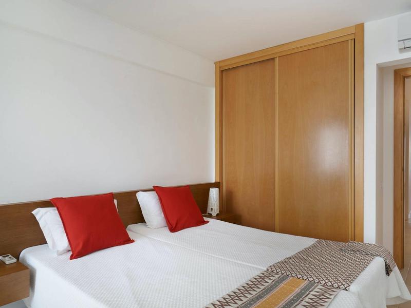 Schlicht eingerichtetes Schlafzimmer mit Doppelbett, roten Kissen und großem Holzkleiderschrank.