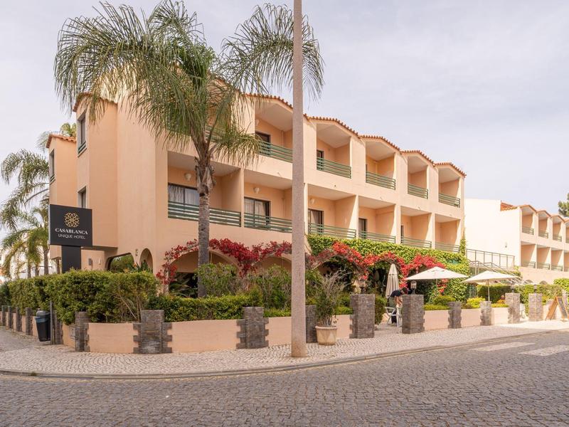 Multi-story hotel building with balconies surrounded by palm trees under a cloudy sky.