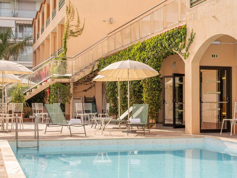 A quiet hotel pool with lounge chairs and umbrellas next to a sandstone building with climbing plants