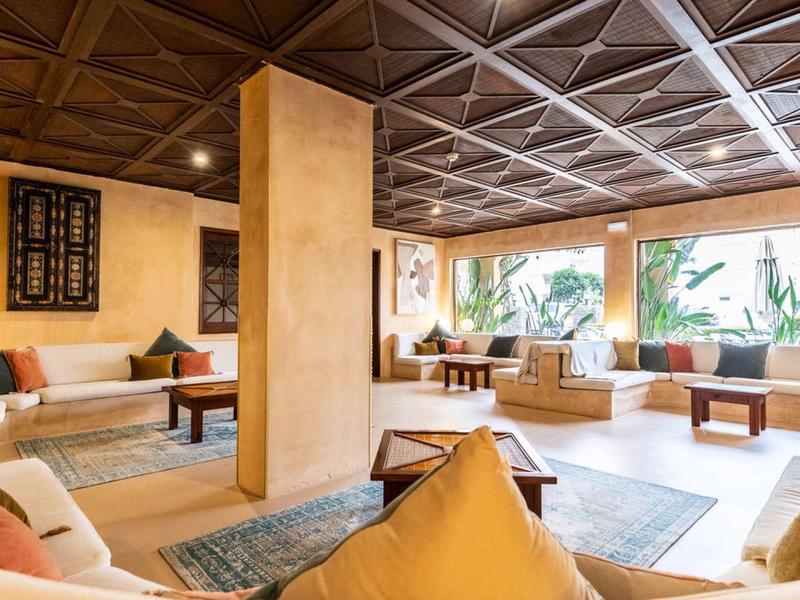 Cozy hotel lounge with wooden ceiling, seating areas, and large windows overlooking plants.