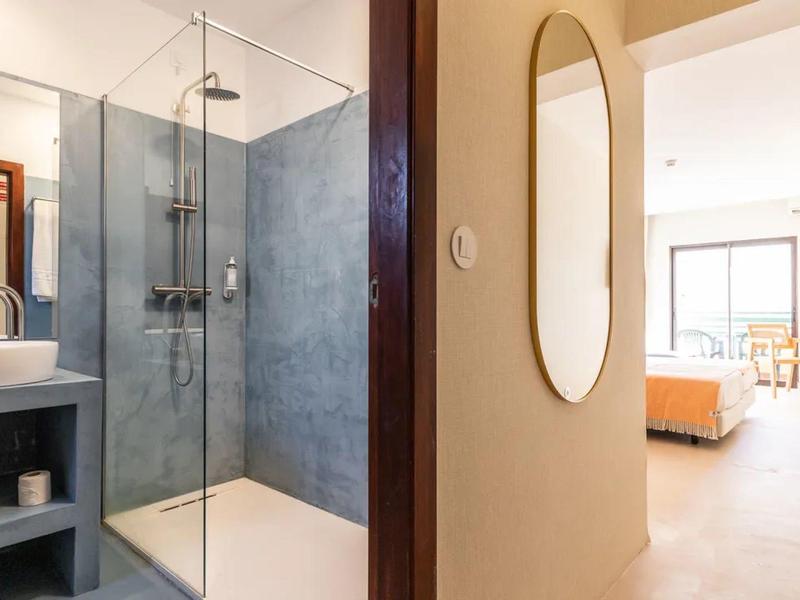Modern hotel bathroom area with shower and view into bright bedroom.