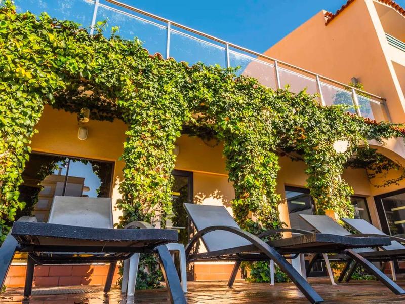 Sun loungers in front of an ivy-covered hotel with an orange facade and glass railing.