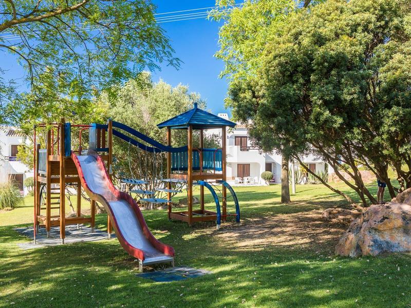 Speeltuin met glijbaan en klimrek in de schaduwrijke tuin van een hotel.