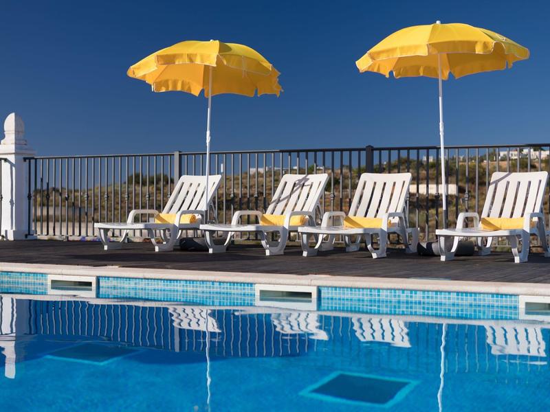 Gele parasols en ligstoelen bij een zwembad onder een heldere blauwe lucht.