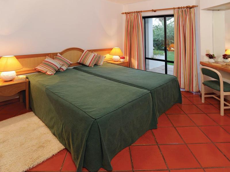 Gezellige hotelkamer met twee eenpersoonsbedden, groene beddengoed en uitzicht op terras.