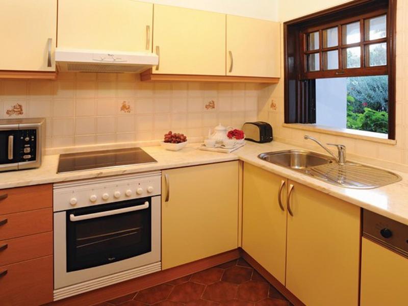 Gezellige keuken met gele kasten, fornuis, magnetron en raam met uitzicht.