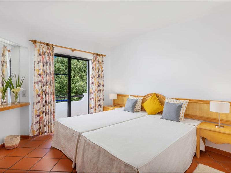 Lichte hotelkamer met twee eenpersoonsbedden, kleurrijke kussens en balkon met uitzicht op groen.