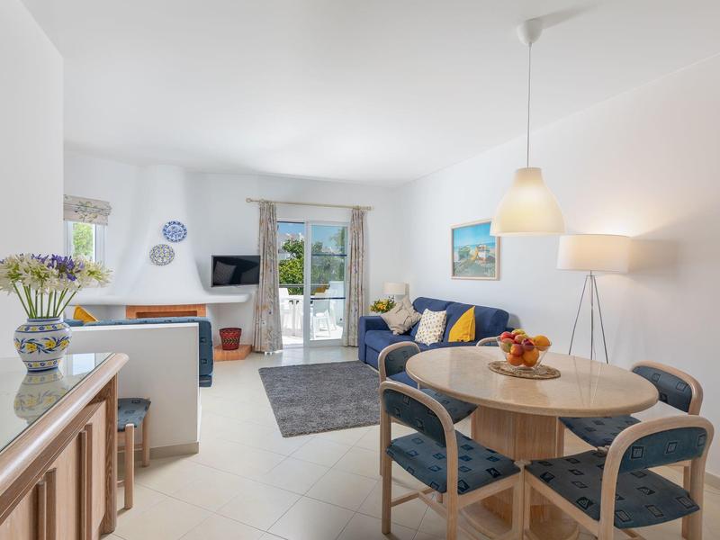 Lichte woonkamer met bank, eettafel, flatscreen-tv en toegang tot terras met zeezicht.