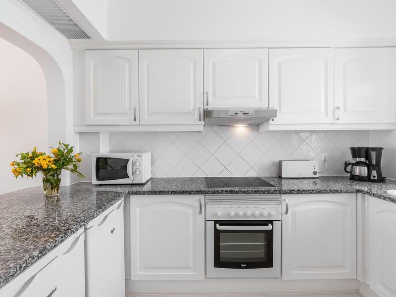 Moderne witte keuken met granieten aanrecht, boeket, magnetron, oven en koffiemachine.