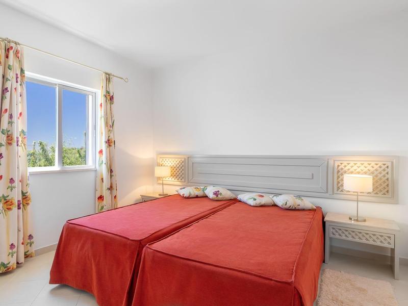 Lichte hotelkamer met twee eenpersoonsbedden, rode bedspreien en ramen met uitzicht op groene bomen.