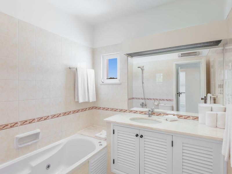 Lichte badkamer met bad, grote spiegels en witte kast onder de wastafel.