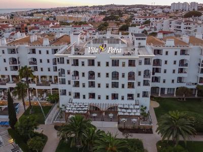 Biały hotel z tarasami i widokiem na miasto o zachodzie słońca.