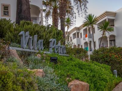 Begrüßungsschild von Vila Park mit weißen Gebäuden und Palmen im Hintergrund.