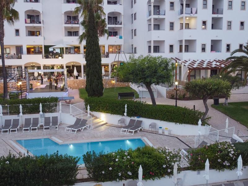 Oświetlony basen hotelowy z leżakami i zielonymi roślinami na dziedzińcu o zmierzchu