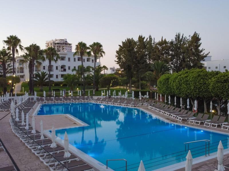 Pusty basen hotelowy otoczony leżakami i palmami o zachodzie słońca.