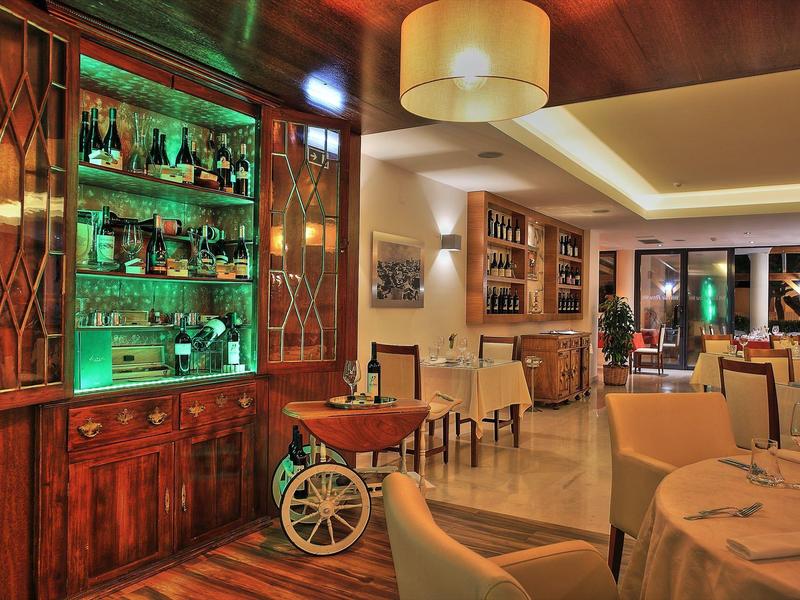 Przytulna część restauracyjna w hotelu z drewnianymi półkami, oświetlonymi napojami i zastawionymi stołami.