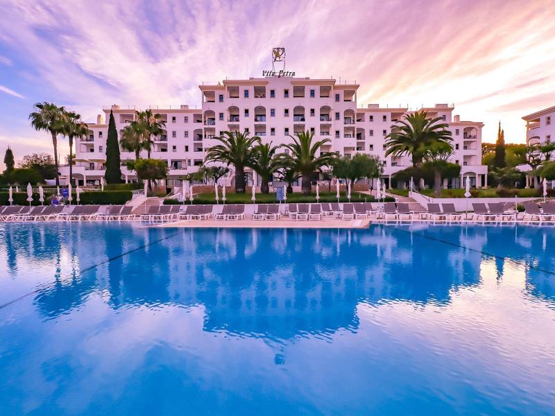 Luksusowy hotel z palmami i dużym basenem o zachodzie słońca.