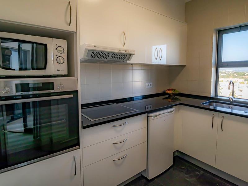 Mała nowoczesna kuchnia z białymi szafkami oraz wbudowanym piekarnikiem i mikrofalówką.