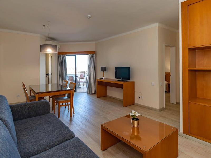 Jasny salon z niebieską kanapą, drewnianym stolikiem, stołem jadalnym i balkonem z widokiem na zewnątrz.