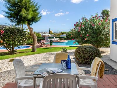 Terras met tafel en stoelen bij een zwembad in een tuinomgeving op een zonnige dag.