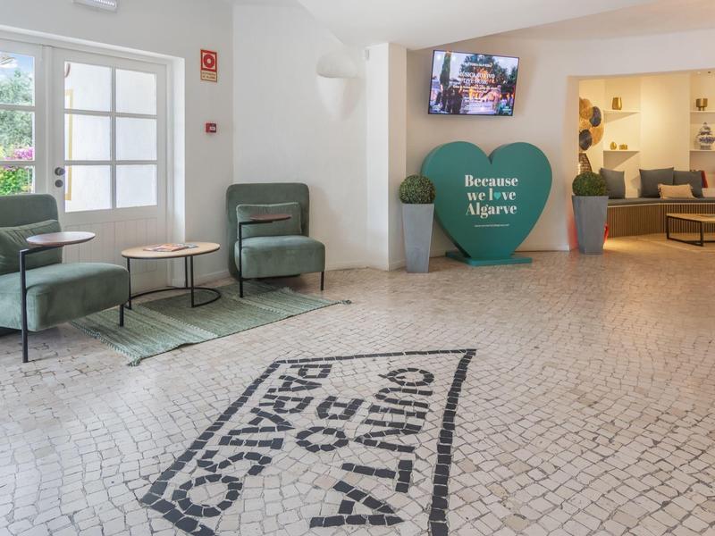 Lichte hotellobby met groene stoelen en een grote hartdecoratie met een welkomstboodschap.
