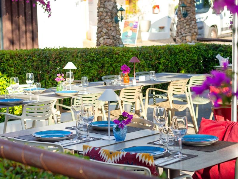 Buitenrestaurant met gedekte tafels, bloemen en stoelen in een zonnige tuin.