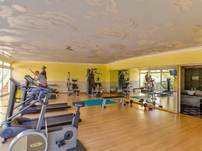 Jasna siłownia z żółtymi ścianami, bieżniami i ścianą lustrzaną.