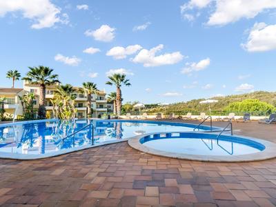 Duży basen na zewnątrz i mała wanna z hydromasażem w kompleksie hotelowym w słoneczny dzień.