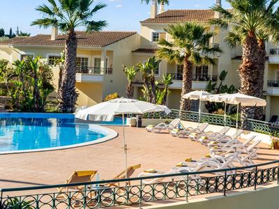 Zewnętrzny basen z leżakami i palmami w ośrodku hotelowym.