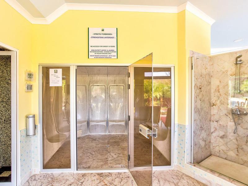 Wejście z żółtymi ścianami, szklanymi drzwiami obrotowymi i marmurową podłogą.