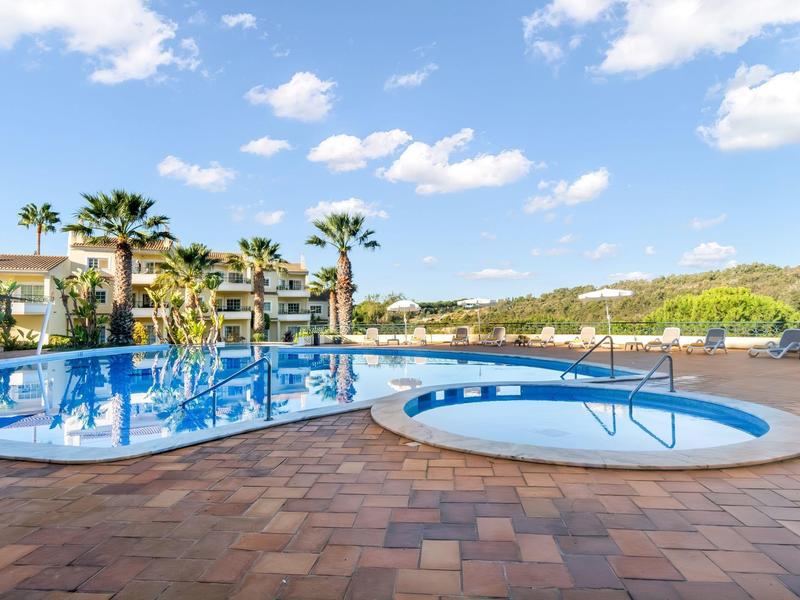 Duży basen na zewnątrz i mała wanna z hydromasażem w kompleksie hotelowym w słoneczny dzień.