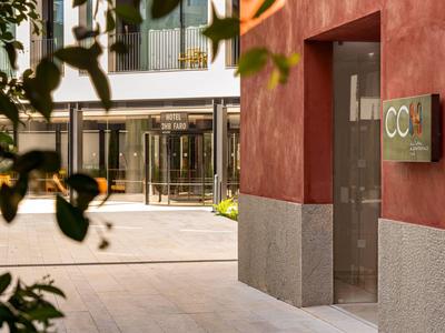 Wejście do budynku z czerwoną elewacją i szyldem, nowoczesny dostęp do hotelu w tle.