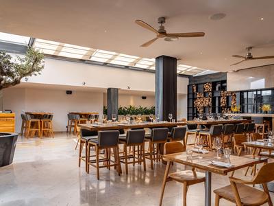 Nowoczesna restauracja z drewnianymi meblami, dużym oknem i wentylatorami sufitowymi w otwartej przestrzeni.