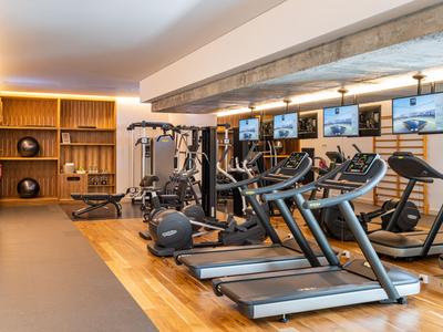 Nowoczesna siłownia z bieżniami i sprzętem do ćwiczeń siłowych, drewniane ściany i duże lustra.