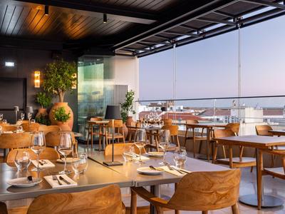 Nowoczesna restauracja z drewnianymi meblami i widokiem na morze o zachodzie słońca.