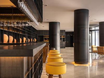 Nowoczesny bar hotelowy z żółtymi stołkami i eleganckimi szklanymi półkami w ciepłym świetle.